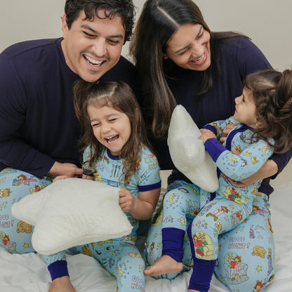 Family smiling with them wearing our PBS Good Night Arthur™ collaboration featuring pajamas adorned with Arthur and friends in a cozy bedtime scene complete with storybooks, toothbrushes, bunny slippers, a sleeping puppy, crescent moons with sleep caps, twinkling stars, and the words "GOOD NIGHT!" on a soft blue background.