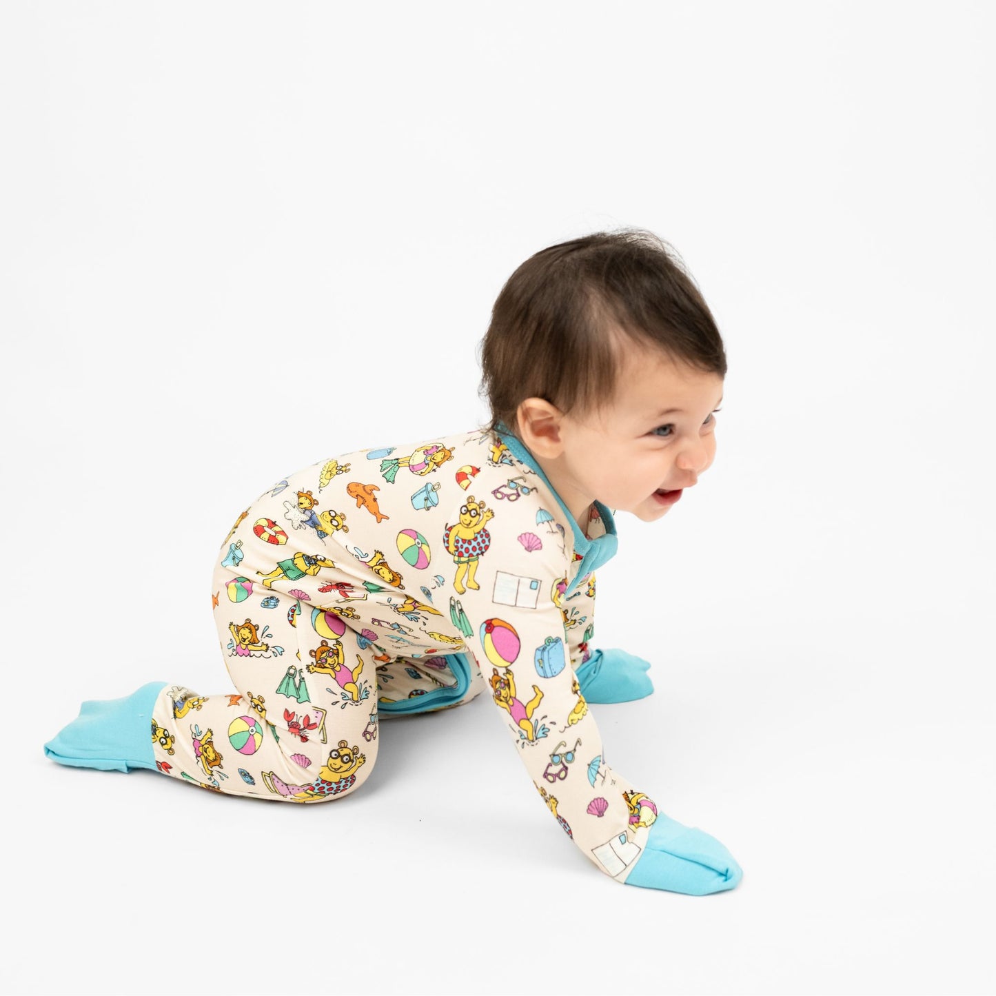 Baby girl crawling and wearing our Arthur's Family Vacation Bamboo Convertible Baby Pajamas featuring vibrant light blue trim, a double zipper, and a playful print of Arthur™ in swimwear surrounded by fun beach props — perfect for family getaways.