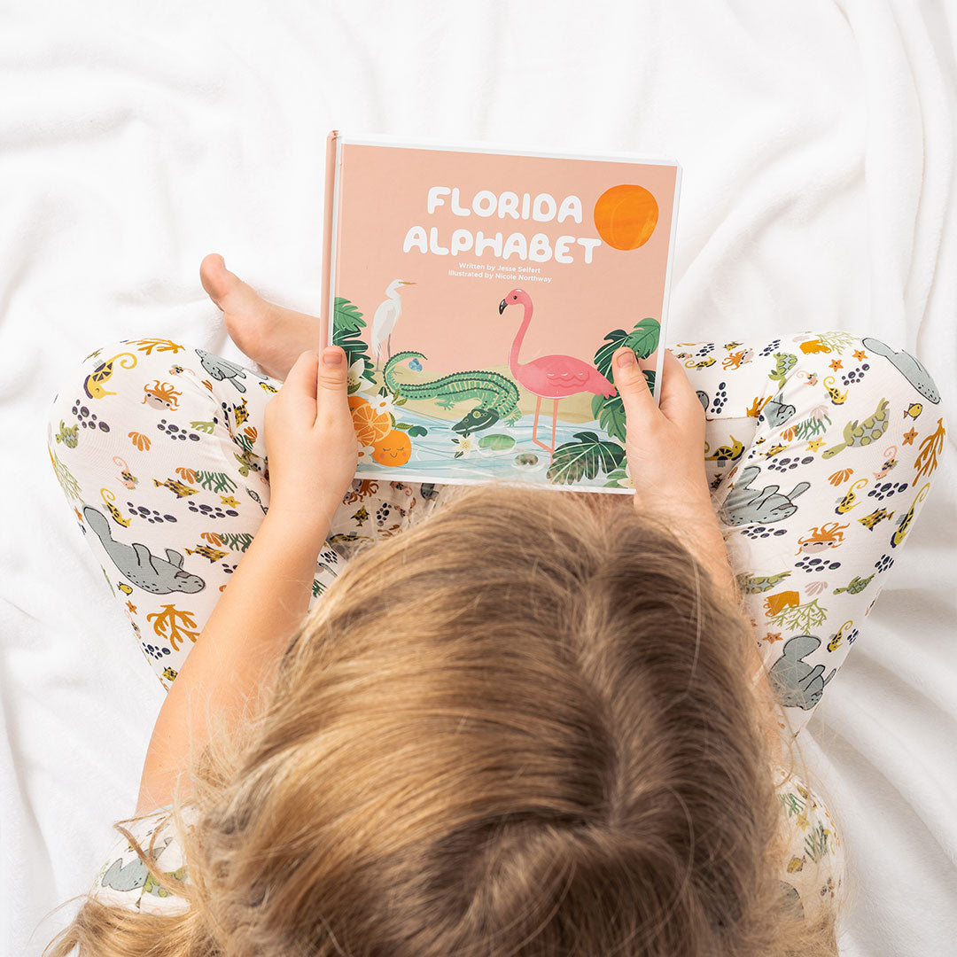 an over head view of a child sitting criss-cross. you can see them holding the Florida Alphabet book.