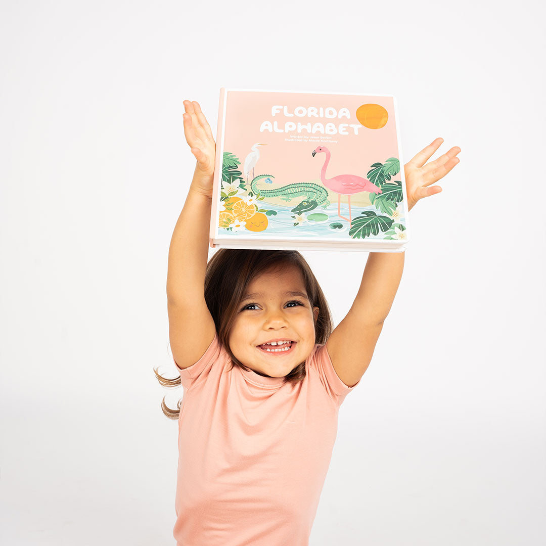 you girl holds the Florida Alphabet book above her head. she smiles wide.