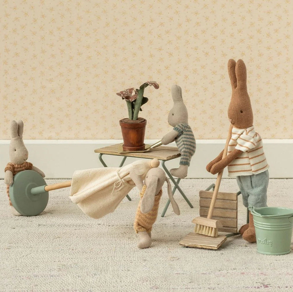 Miniature scene with toy bunnies engaged in cleaning activities on a wooden floor.
