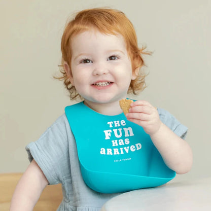 toddler eating a snack wearing a blue silicone bib that says the fun has arrived