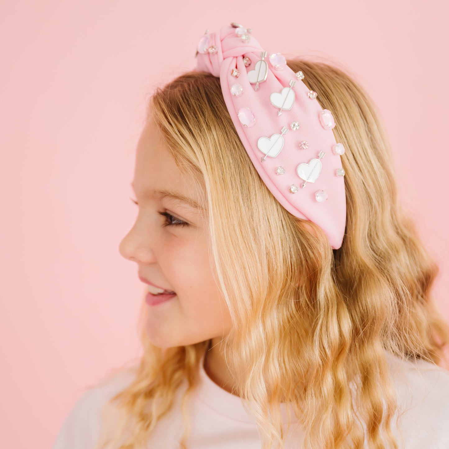 Young girl wearing a pink headband with heart decorations on a pink background