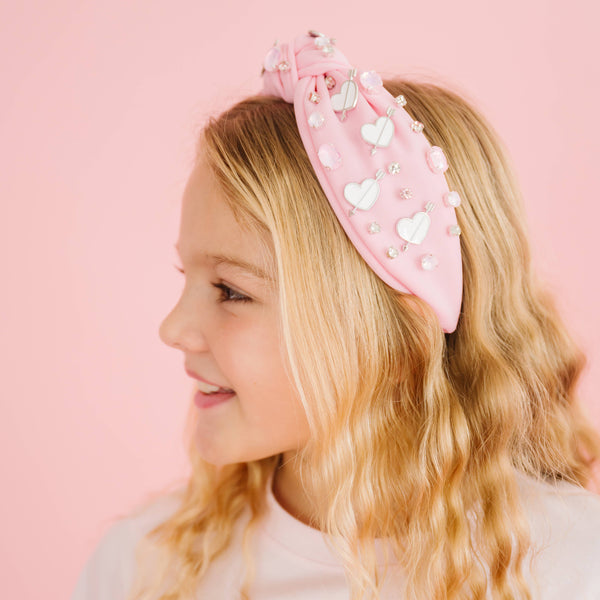 Young girl wearing a pink headband with heart decorations on a pink background