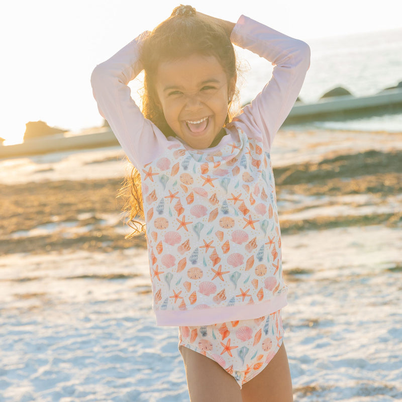 Girl wearing our sandy Seashlles rashguard at the beach