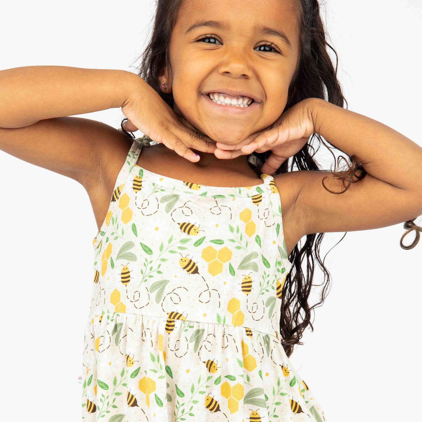 Smiling young girl wearing a soft bamboo sundress with an adorable honey bee print. This hypoallergenic and breathable dress is perfect for spring and summer wear.