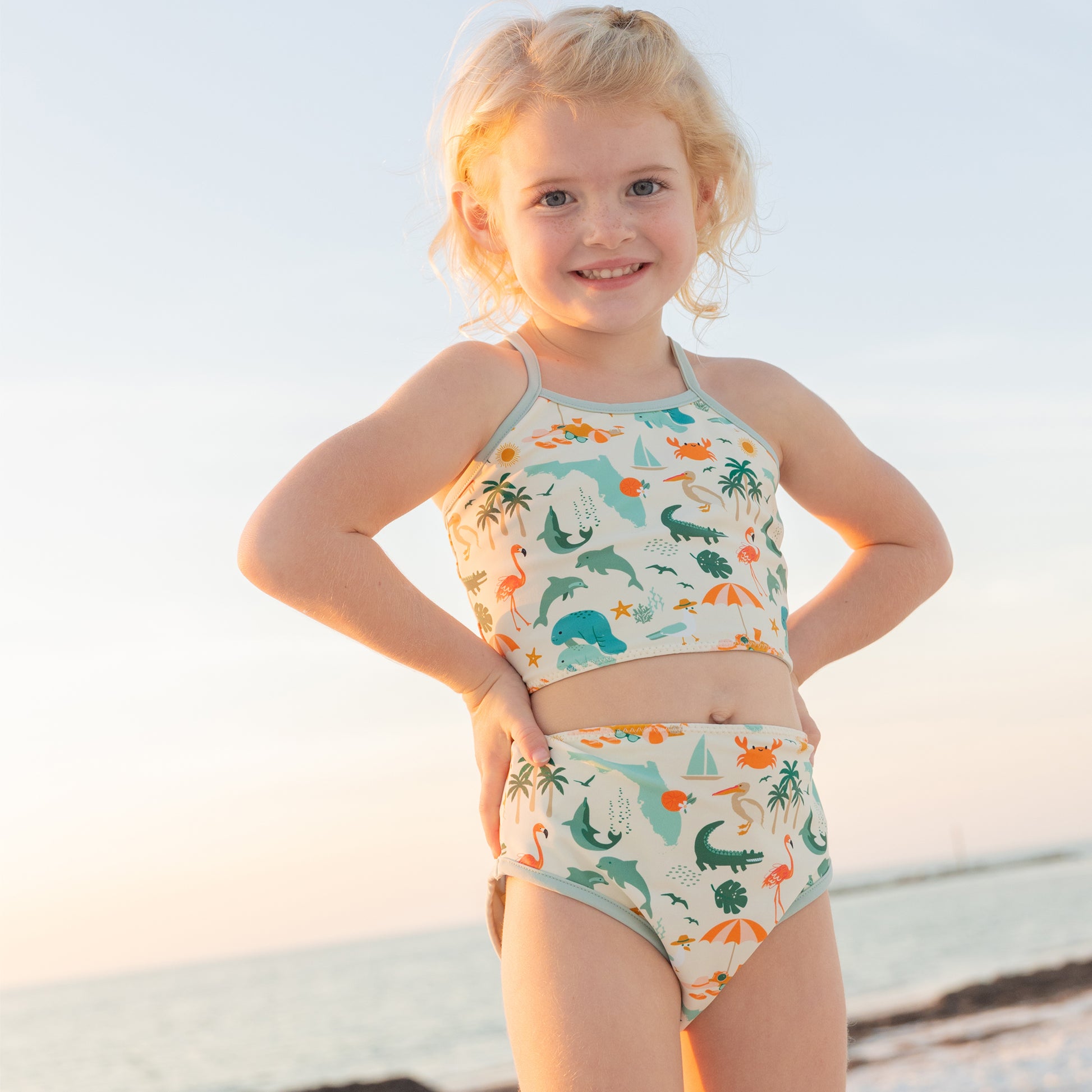 A young girl posing on the beach in the Explore Florida bikini, showcasing the secure crossback tank-style top.