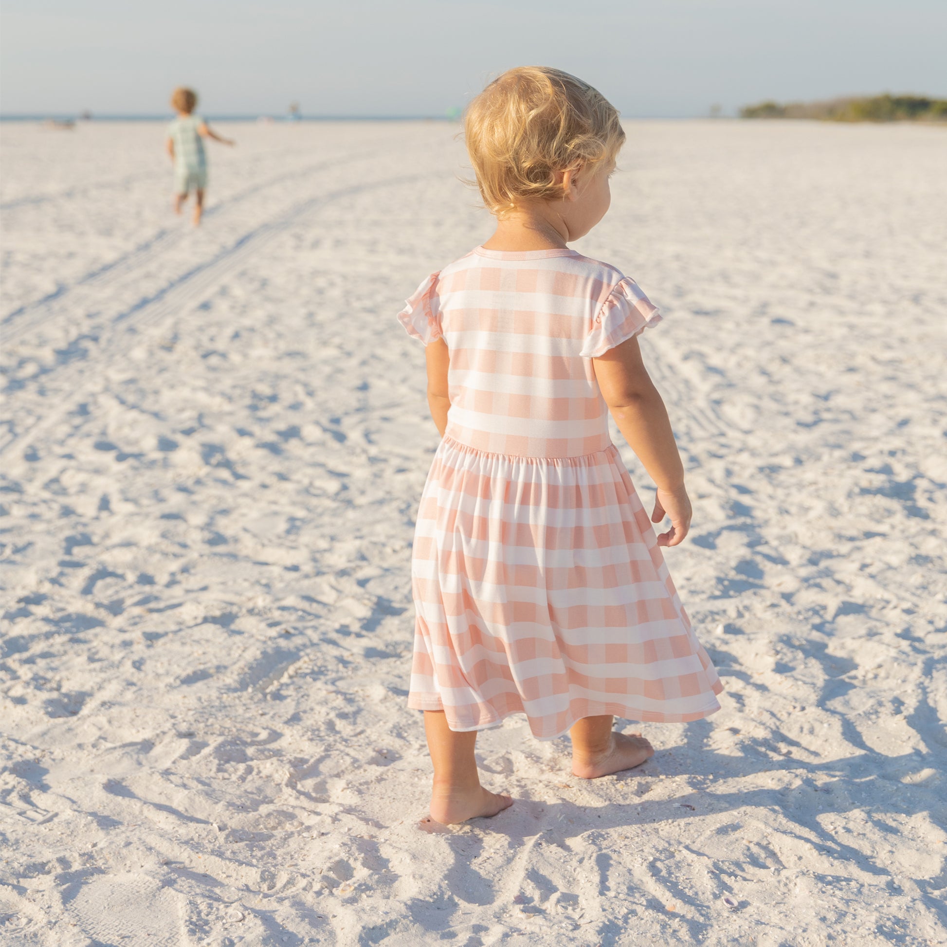 Little girl walking on the beach in a breathable pink gingham bamboo dress designed for spring and summer.