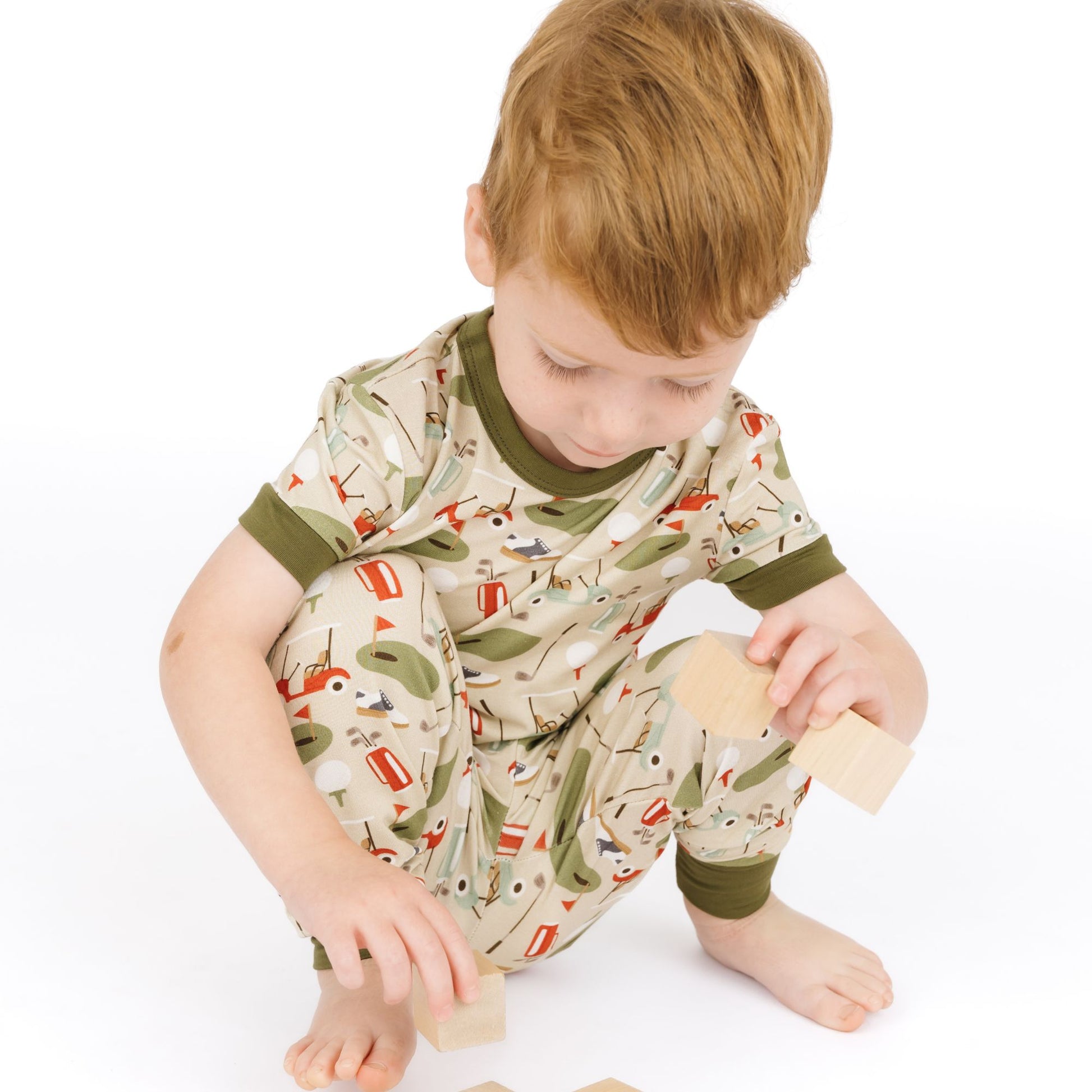 Child wearing a patterned onesie playing with wooden toys on a white background