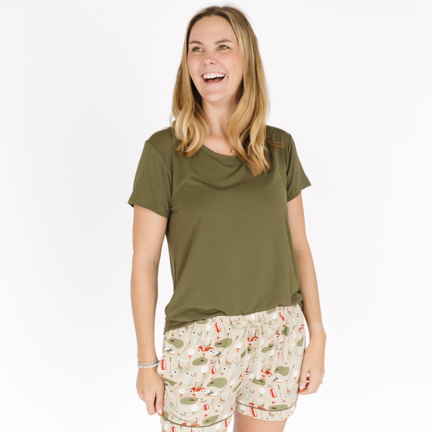 Woman wearing an olive green t-shirt and patterned shorts on a white background