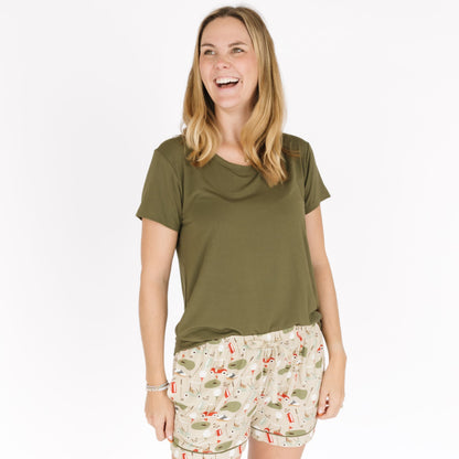 Woman wearing an olive green t-shirt and patterned shorts on a white background