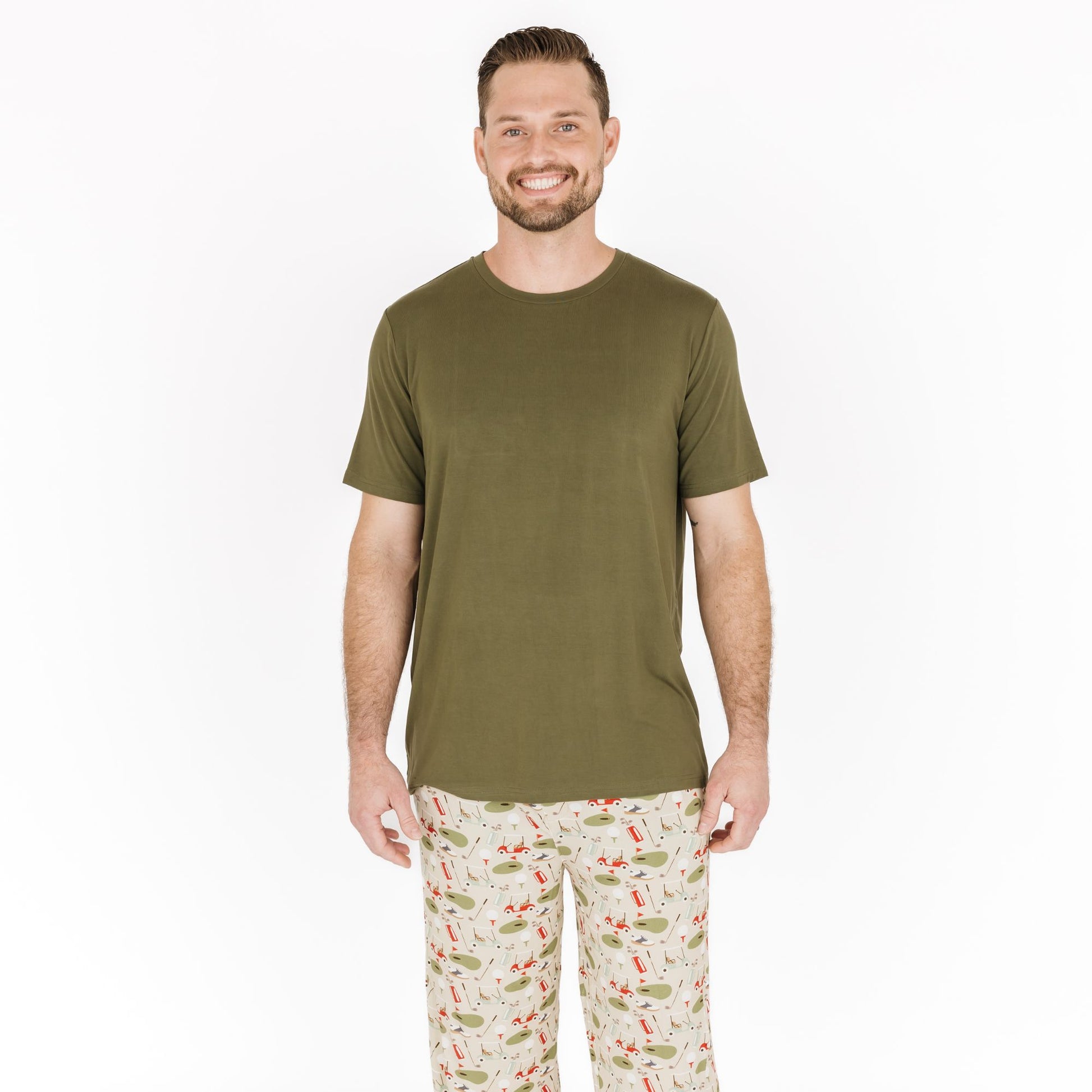 Man wearing an olive green t-shirt and patterned pajama pants on a white background
