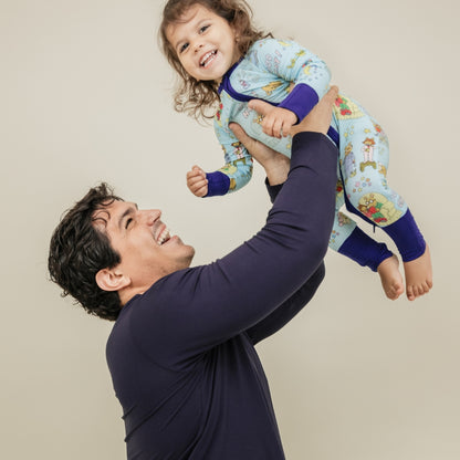A heartwarming moment captures a dad and his smiling daughter, with her wearing our PBS Good Night Arthur™ collaboration featuring pajamas adorned with Arthur and friends in a cozy bedtime scene complete with storybooks, toothbrushes, bunny slippers, a sleeping puppy, crescent moons with sleep caps, twinkling stars, and the words "GOOD NIGHT!" on a soft blue background.