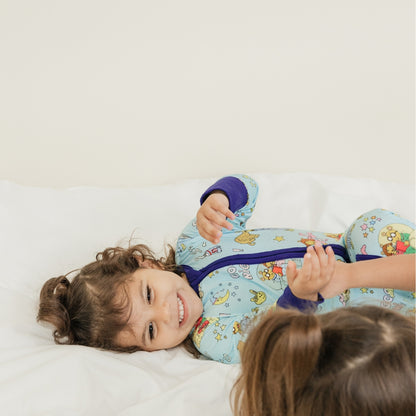Adorable moment with sisters smiling. She is wearing our collaboration with PBS Good Night Arthur™ pattern. The pajama features Arthur and friends in a cozy bedtime scene with storybooks, toothbrushes, bunny slippers, a sleeping puppy, crescent moons wearing sleep caps, twinkling stars, and the words "GOOD NIGHT!" on a soft blue background.
