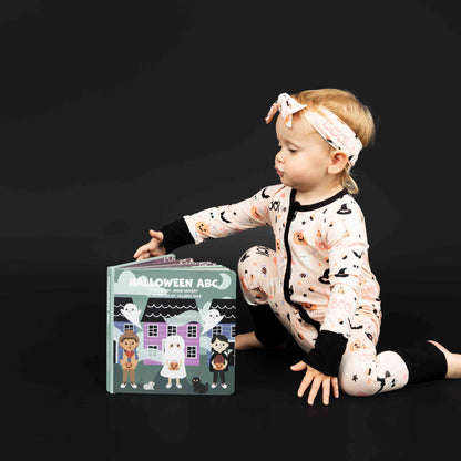 Girl sitting with Halloween ABC board book propped in front of her. SHe is modeling our Sweet and Spooky bamboo pajama print