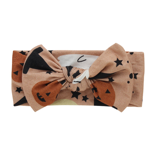 the "trick or treat" baby headband. the "trick or treat" print is a mix of ghost, black cats, pumpkins, witches hats, and stars scattered around a orange background. 