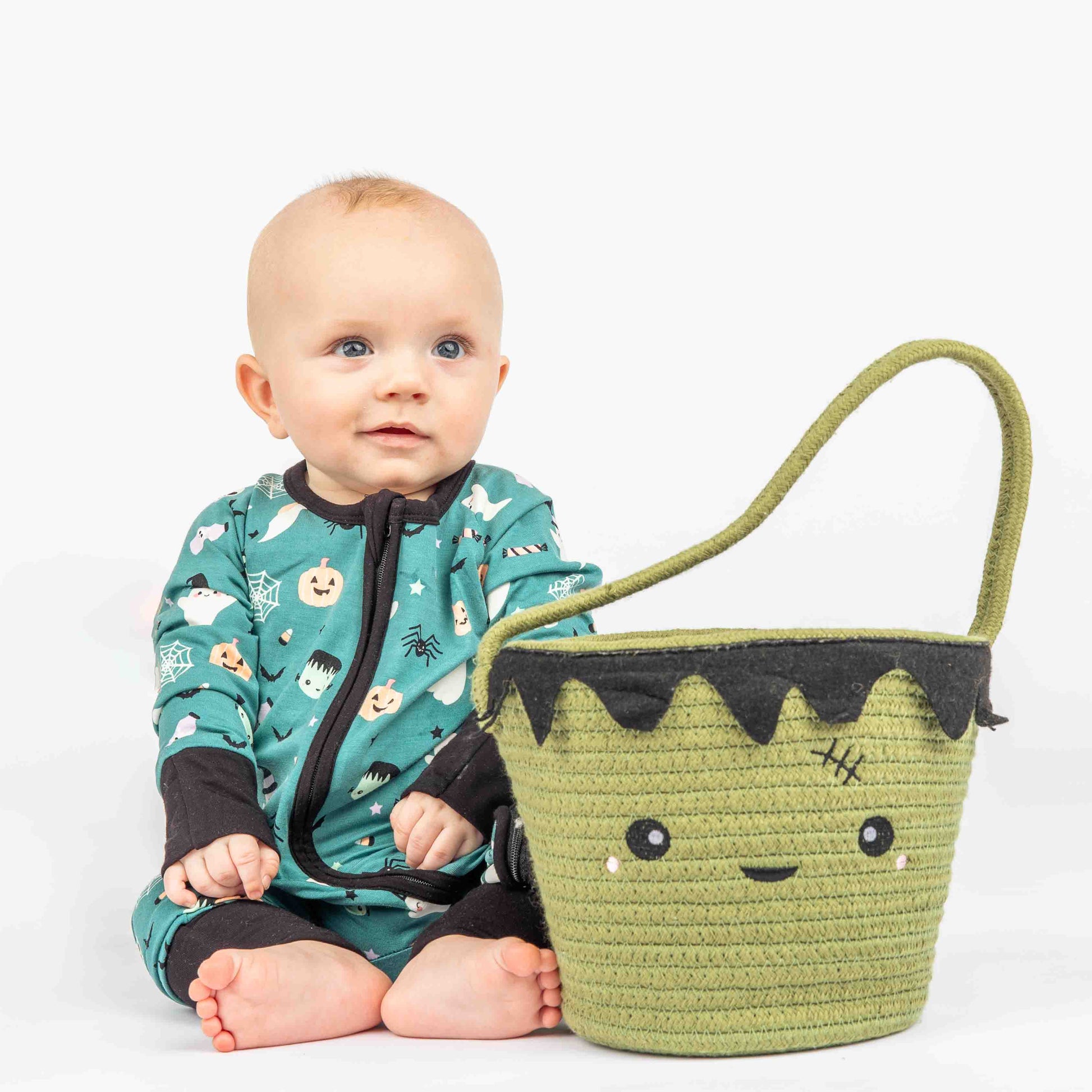 Baby Sitting and smiling sitting next to a Frankenstein Rope Halloween basket modeling "Boo Crew" our halloween print featuring glow in the dark white ghosts and stars, pumpkins, spiders, webs, candy, Frankenstein, and more!