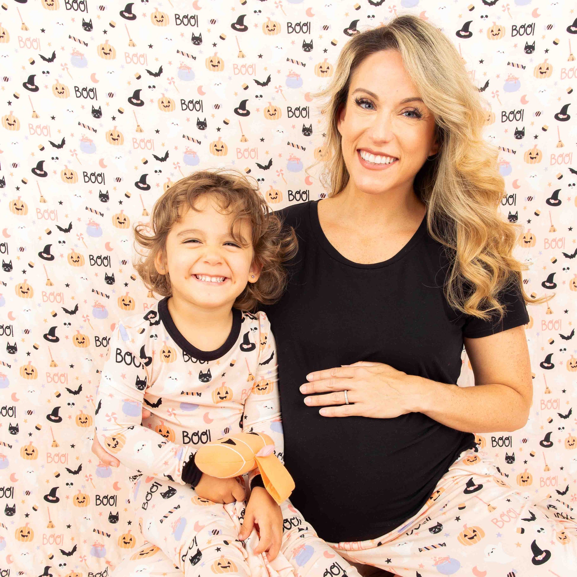 Mom and daughter sitting in their sweet and spooky pajamas while sitting in front of the big bamboo blanket in our Sweet and Spooky pink halloween Print featuring glow in the dark patterns, pumpkins, candy, bats and more!