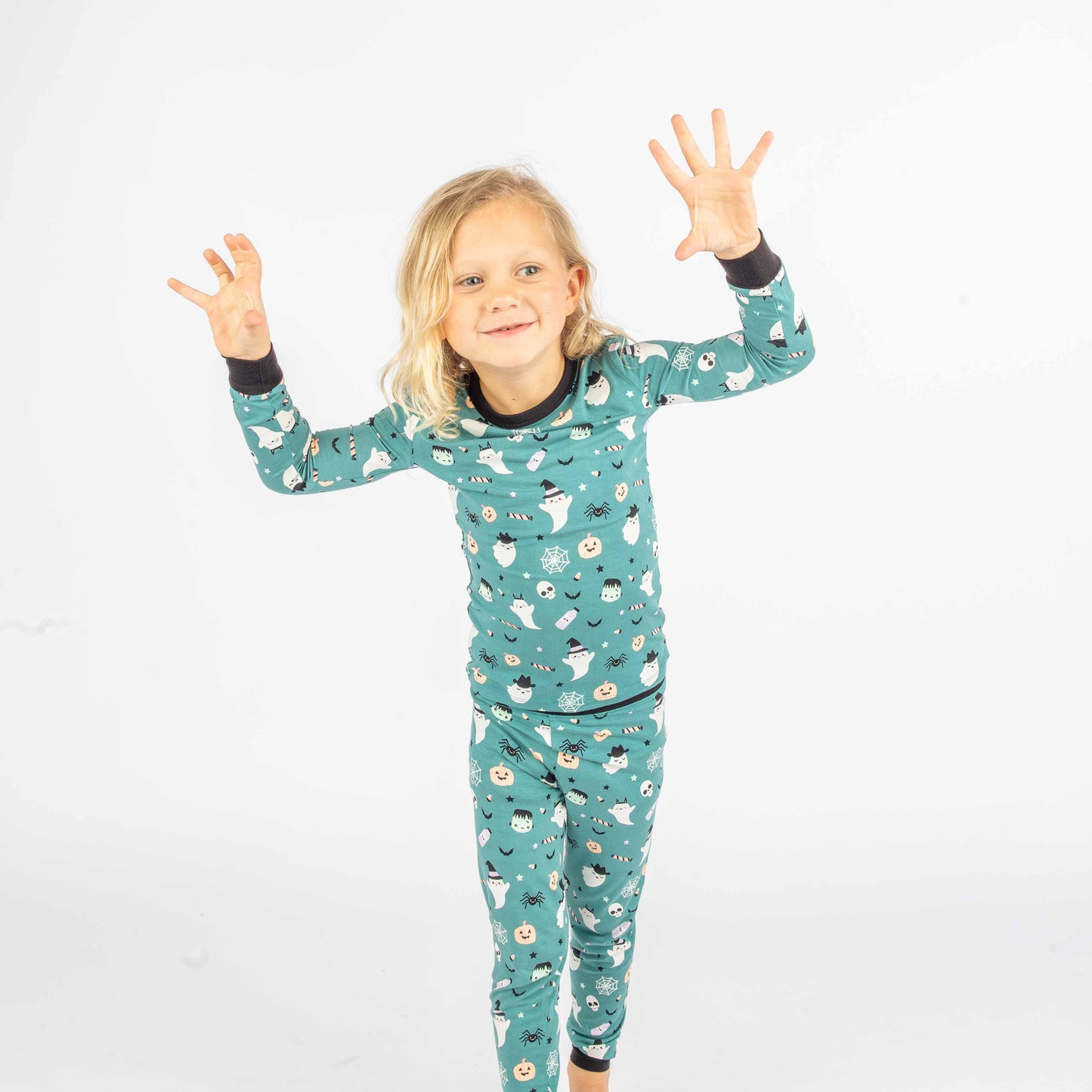 Kid holding up spooky monster hands while wearing the kids pajama long sleeve set in the "Boo Crew" our halloween print featuring glow in the dark white ghosts and stars, pumpkins, spiders, webs, candy, Frankenstein, and more!