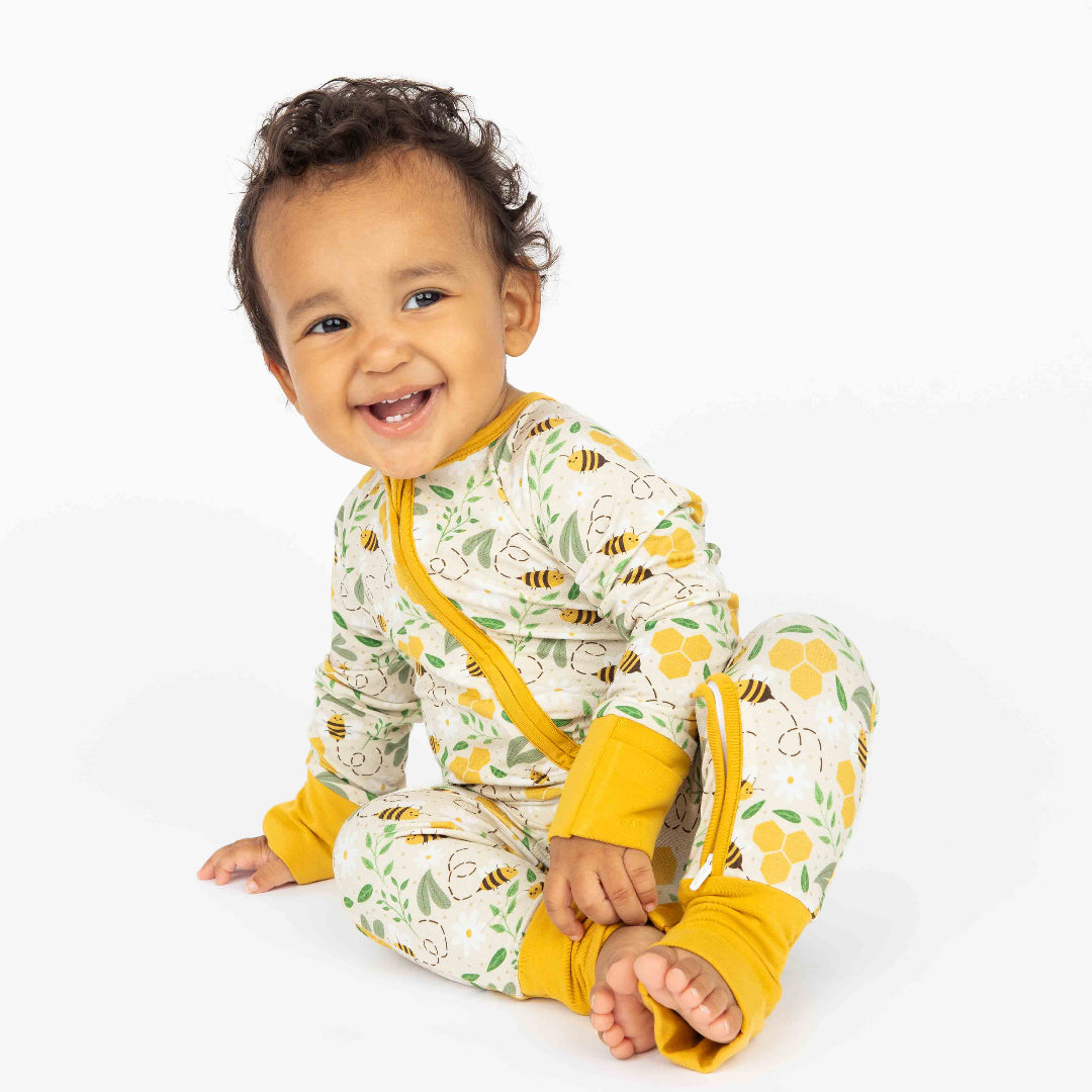 A baby smiling while wearing soft, breathable, and hypoallergenic bamboo convertible pajamas featuring a cute honey bee print.