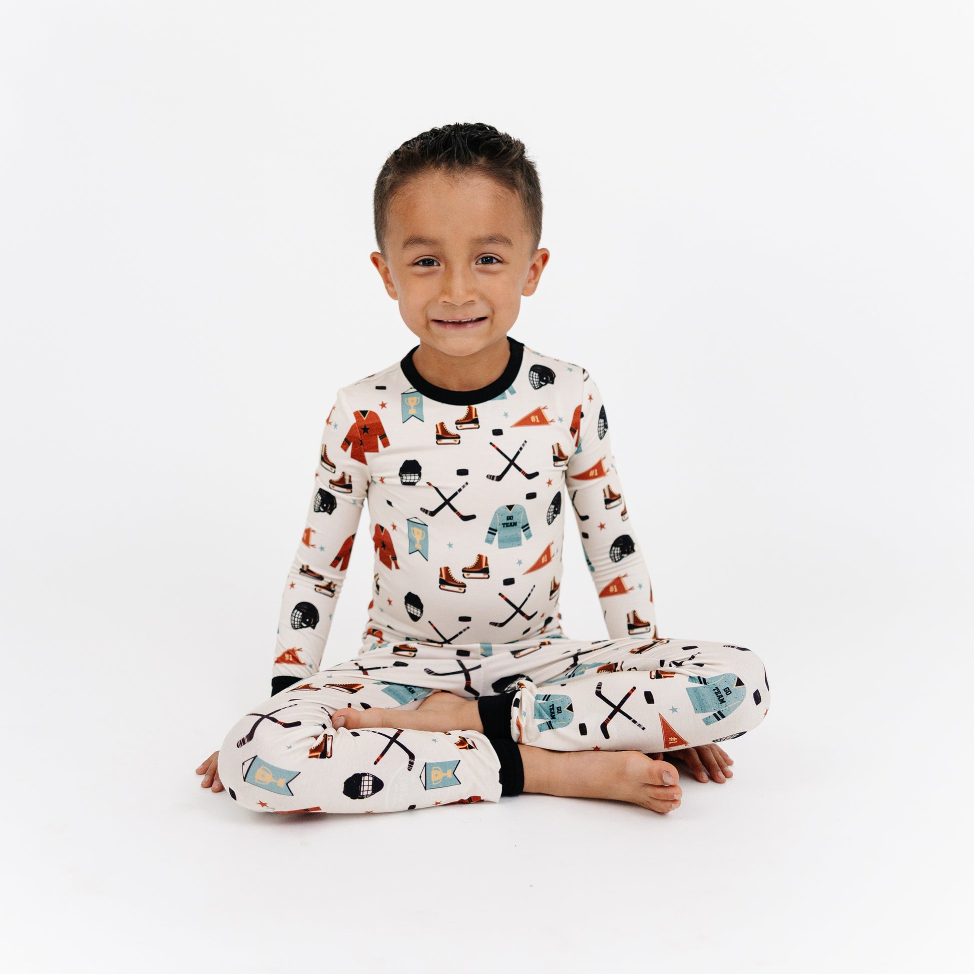 Child wearing pajamas with a pattern of skis, snowflakes, and other winter elements on a white background.