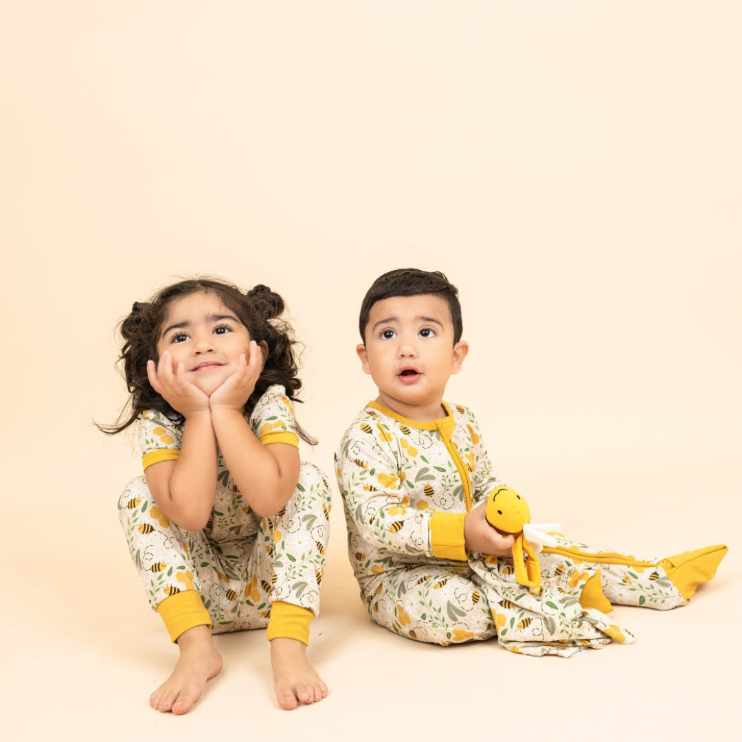 A toddler boy and girl sitting together in soft bamboo pajamas with a honey bee and honeycomb print, cozy and perfect for bedtime.