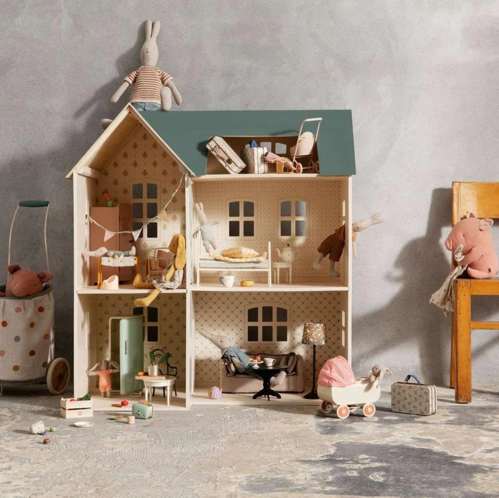 Dollhouse with miniature furniture and toys on a textured floor against a gray wall.