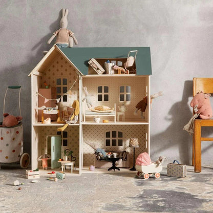 Dollhouse with miniature furniture and toys on a textured floor against a gray wall.
