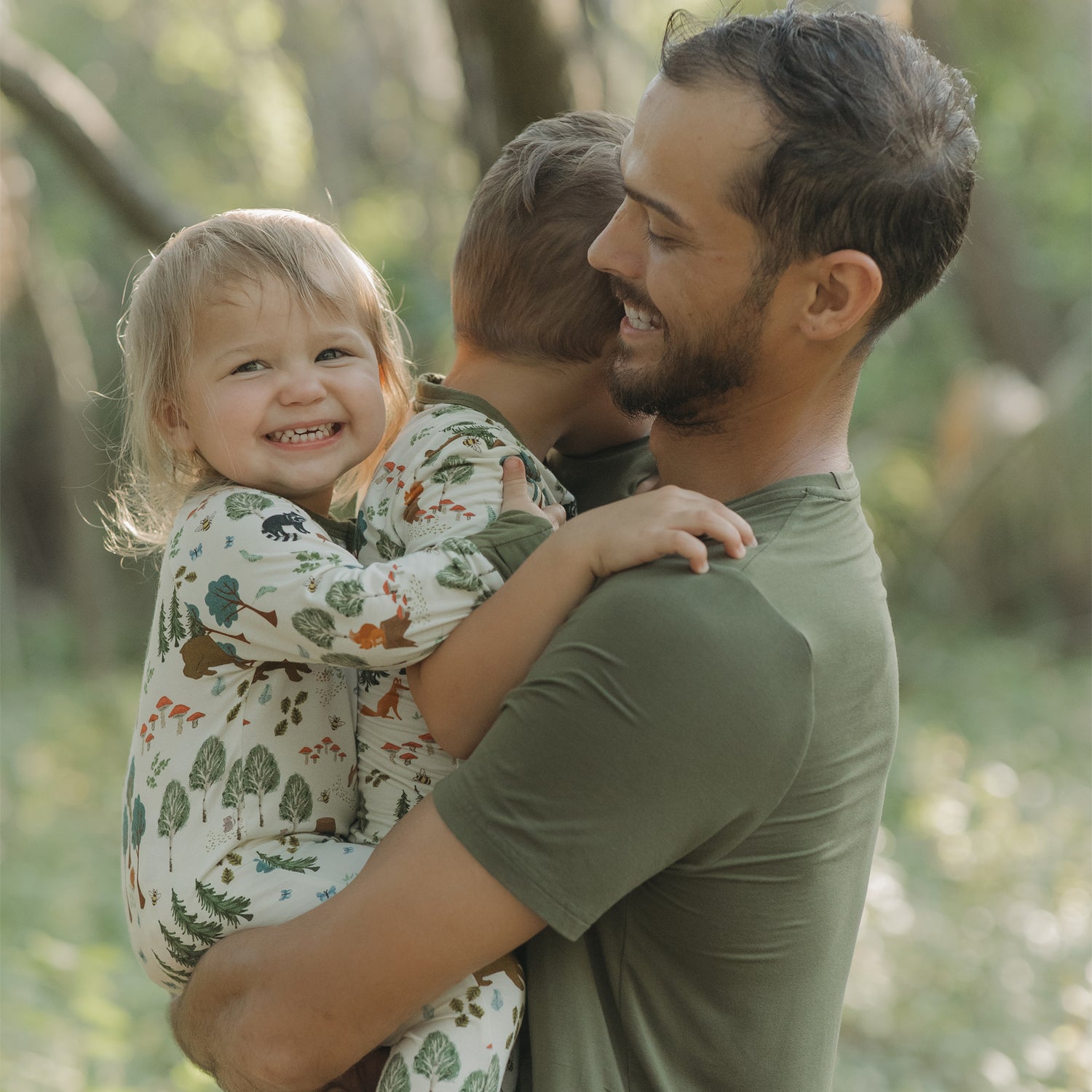 Man holding two children outdoors with a natural background