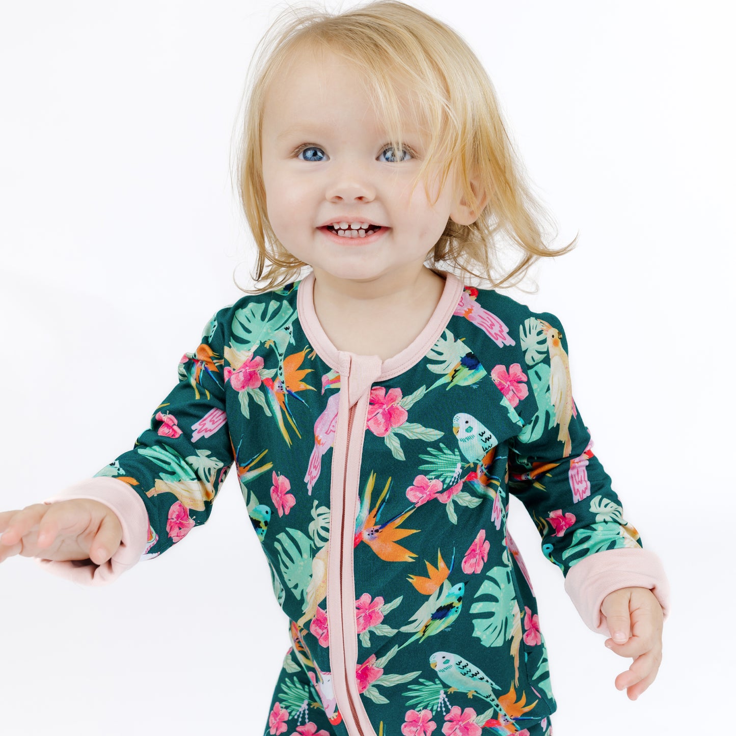 Medium shot of a baby girl in the Isla Botánica botanical island print bamboo romper with easy-access zipper.