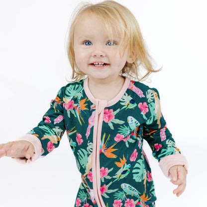 Medium shot of a baby girl in the Isla Botánica botanical island print bamboo romper with easy-access zipper.