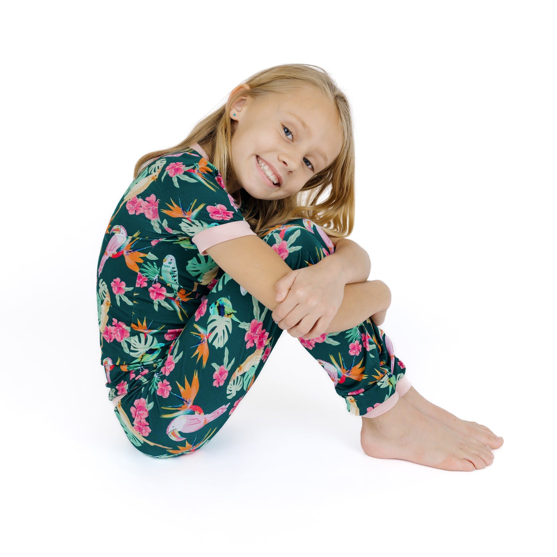 Child sitting comfortably in the Isla Botánica tropical birds print pajamas, highlighting the lightweight and moisture-wicking fabric.
