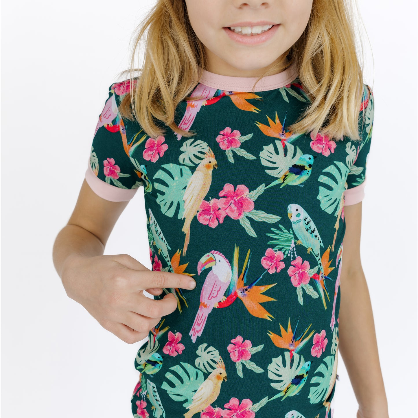 Medium shot of a girl in the Isla Botánica short sleeve pajamas, featuring vibrant tropical birds and palm leaves.