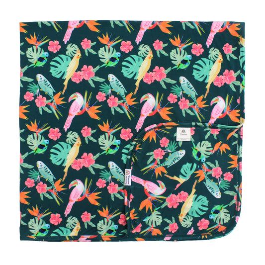 Double-layered luxury bamboo blanket in the Isla Botánica print featuring colorful tropical birds and lush palm leaves.