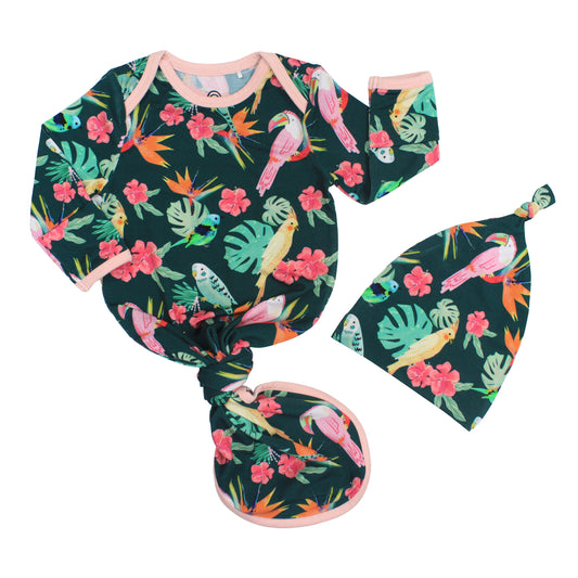 Newborn baby gown and matching knotted hat set in the Isla Botánica print featuring colorful tropical birds and palm leaves.