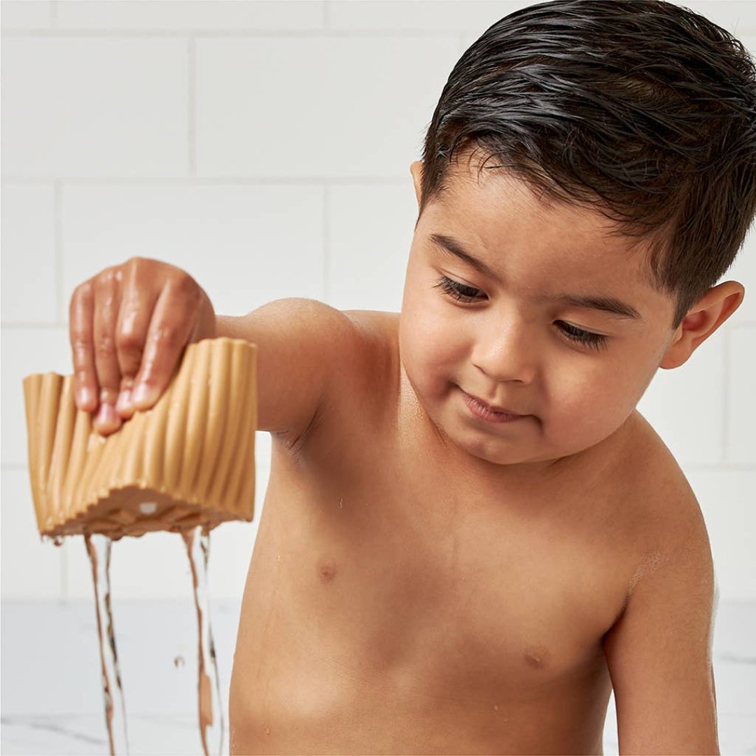 little boy dripping water out of a silicone stacking block with holes in the bottom of it