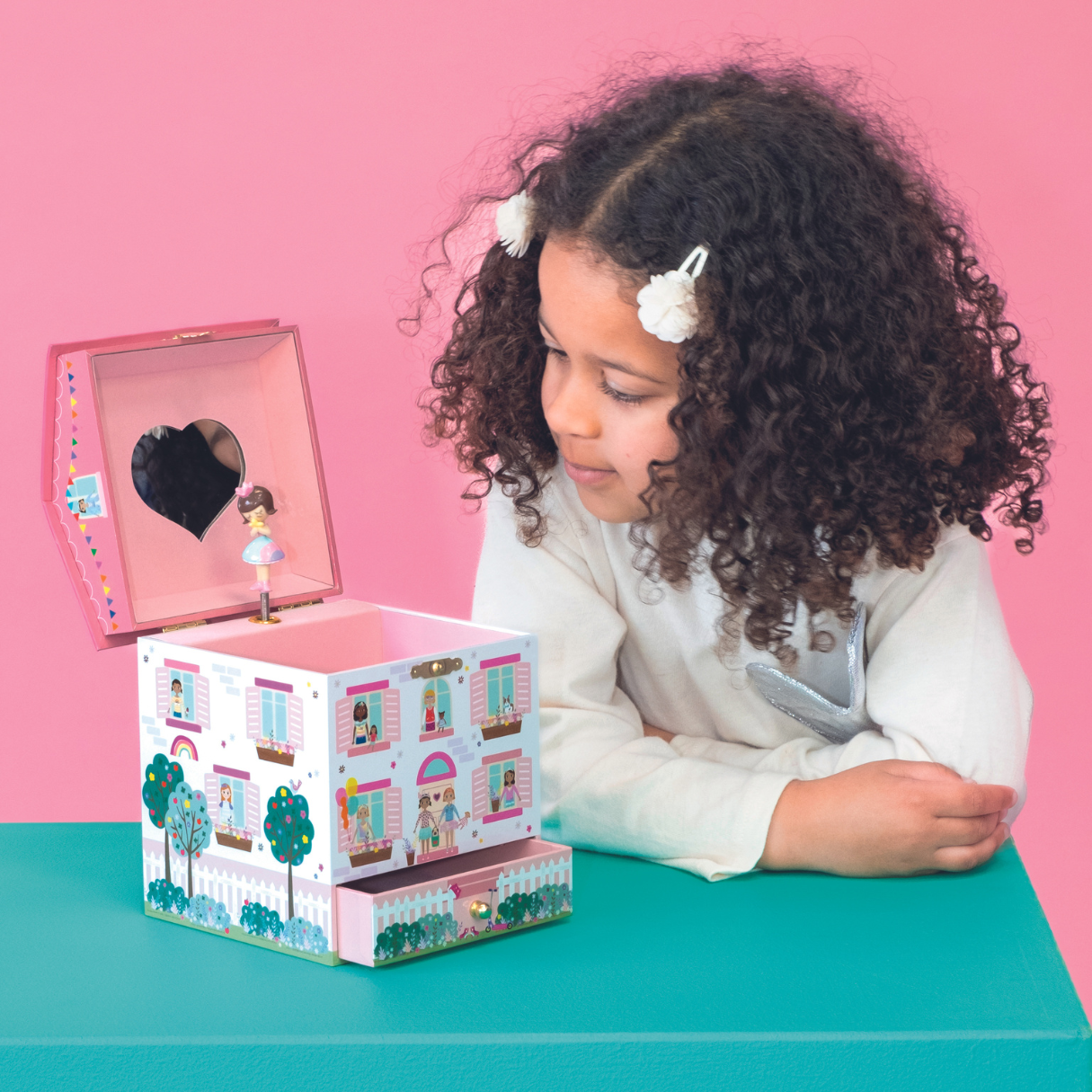 Child playing with a toy music box against a pink background