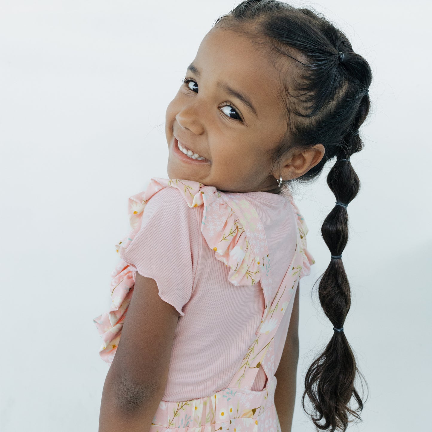 Young girl with braided hair wearing a pink crossback flare leg romper on a white background