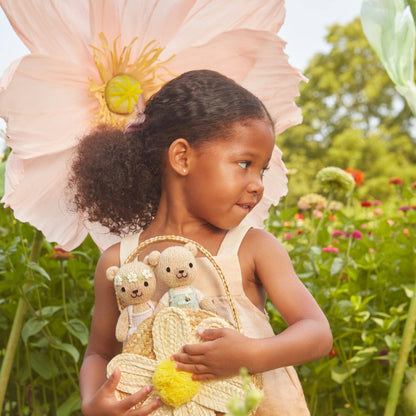 Young girl in a garden holding teddy bears and a basket, with a large flower in her hair.