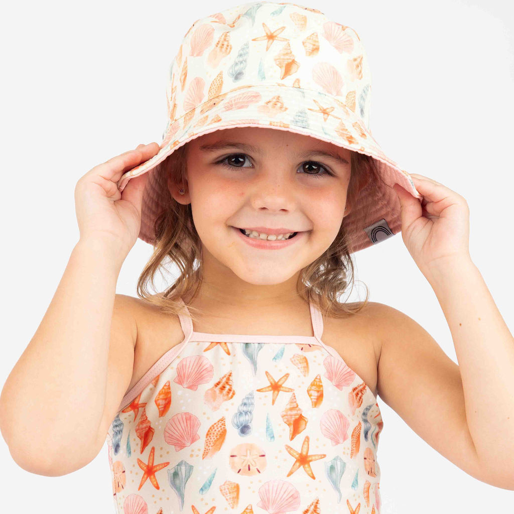 Little girl in sandy seashell bucket hat and bikini