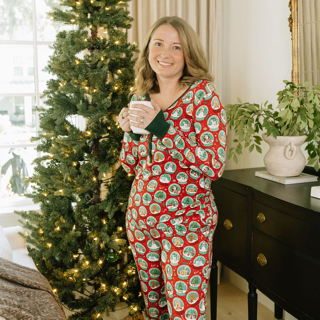 Woman wearing Let It Snow Bamboo Pajama Jogger Pants with a matching holiday pajama top beside a Christmas tree.