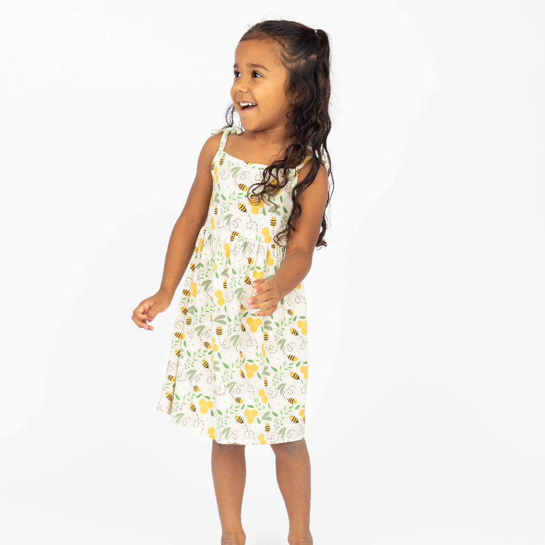 Smiling young girl wearing a lightweight bamboo sundress featuring a honeycomb and bee print. Designed for breathability, comfort, and hypoallergenic softness, perfect for warm-weather adventures.