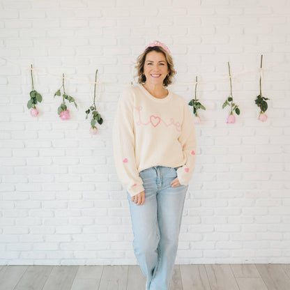 Woman wearing Love knit sweater with pink heart embroidery.
