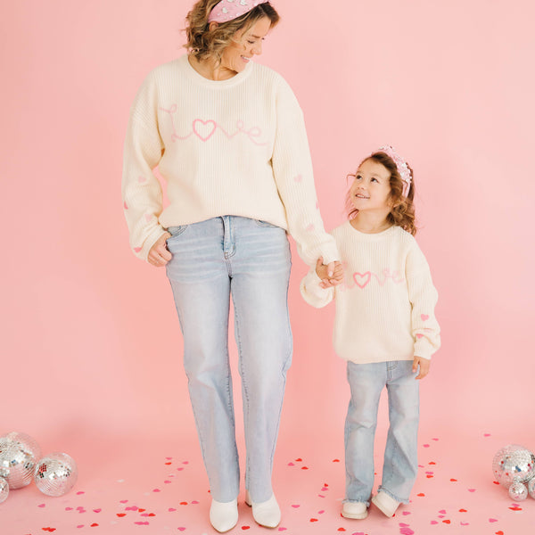 Mama and child wearing matching Love knit sweaters with pink heart details.