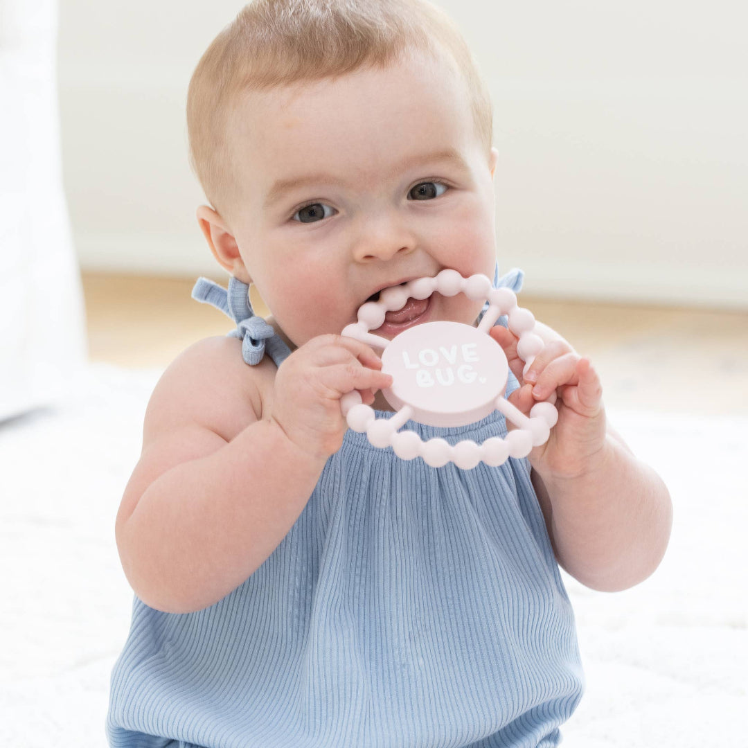 little baby with a light pink round teether that says love bug in white letters