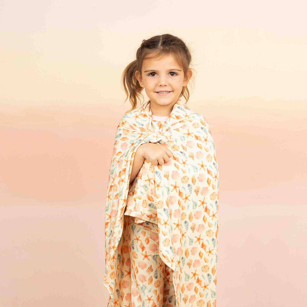 Our luxury bamboo blanket in a sandy seashell print, wrapped around a little girl wearing the same pajamas.