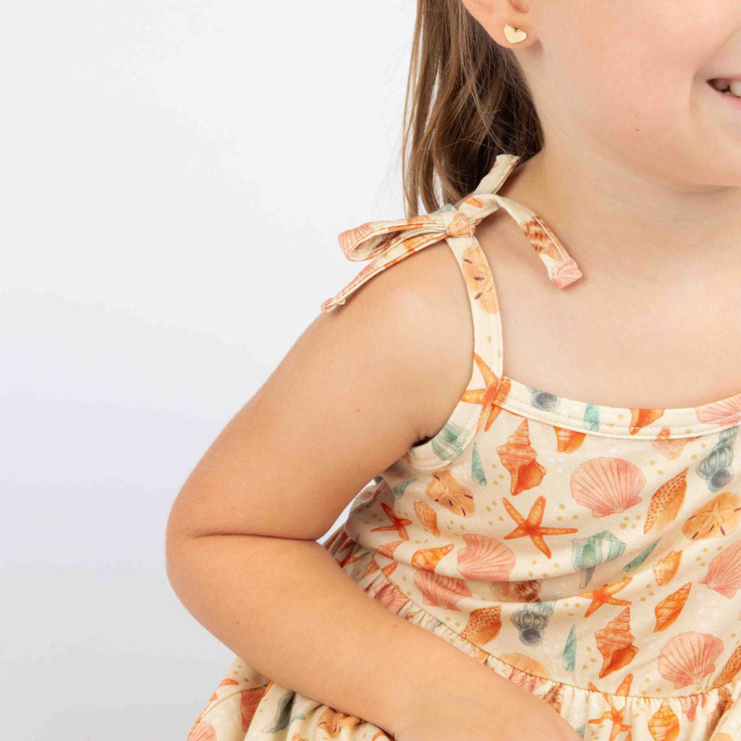 Close up of a Girl smiling and posing with our Sandy Seashell Sundress in a white background. 