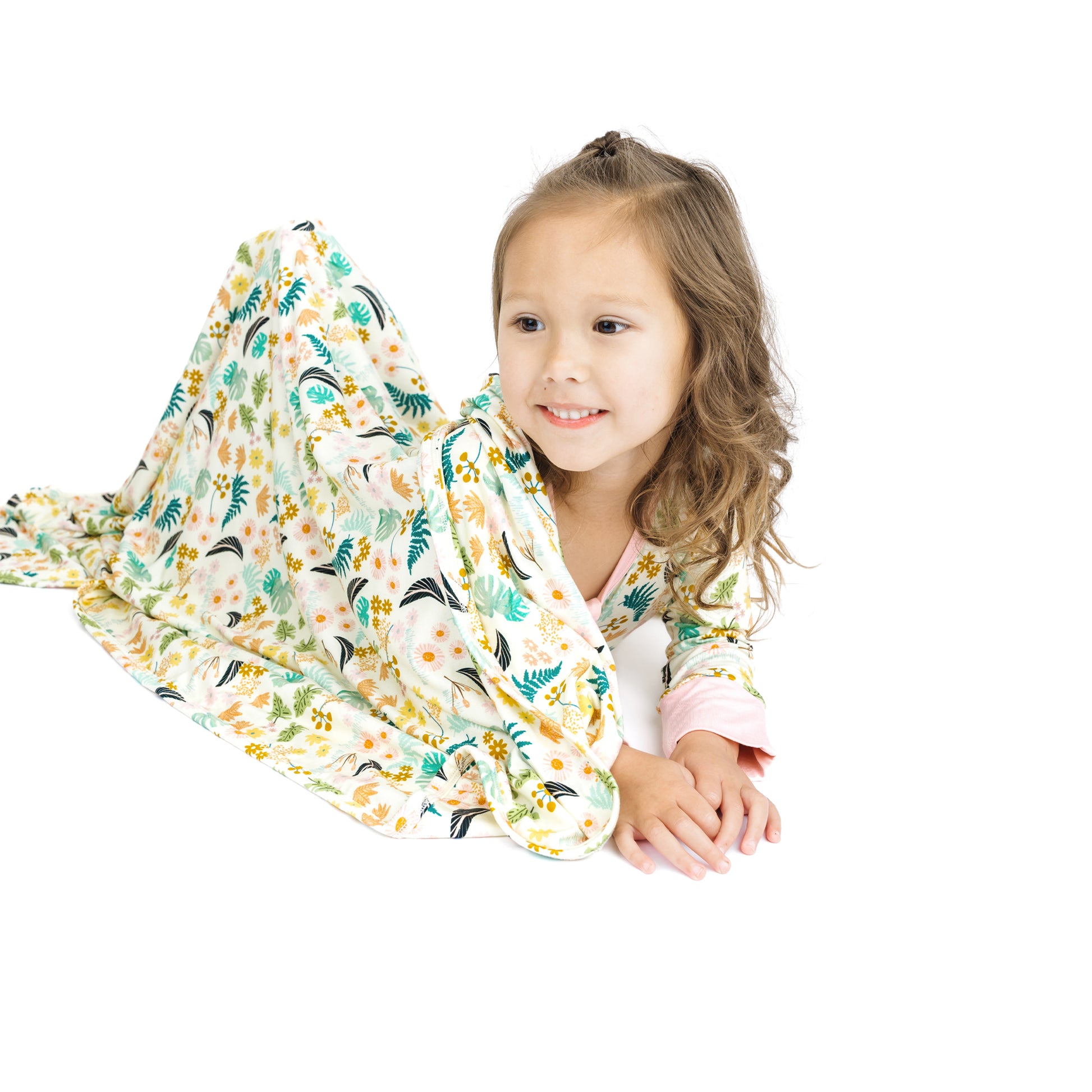 Child laying down on a white background with the Tropical Blooms luxury bamboo blanket, showcasing its generous 40x40 size.