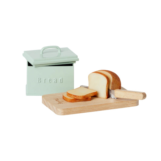 Mint green bread bin with sliced bread on a wooden board with a knife.