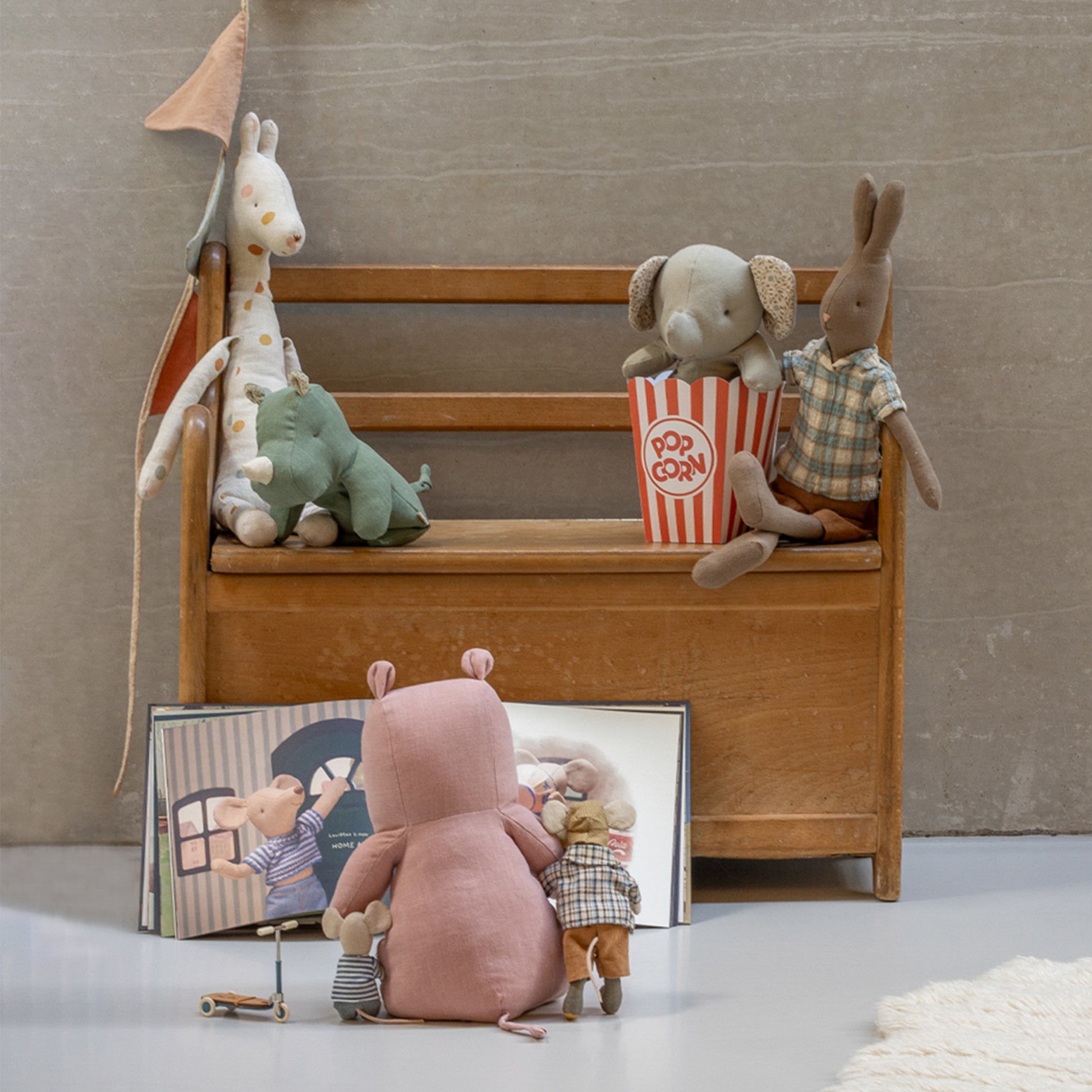 Wooden toy bench with stuffed animals and a book on a neutral background